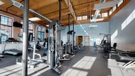 Located at 607 Norwich Ave in Norwich, CT, this fitness center occupies a spacious, single-floor industrial-style building that masterfully blends historic character with modern functionality. The interior is defined by soaring ceilings with warm wood paneling and exposed structural beams, complemented by industrial HVAC ductwork that adds an authentic loft aesthetic. Expansive multi-pane windows line the brick walls on multiple sides, flooding the workout floor with generous natural light and offering views of the surrounding Norwich streetscape.

The main workout area is generously proportioned, accommodating a comprehensive selection of equipment including treadmills, stationary bikes, ellipticals, rowing machines, cable systems, free weights, and multi-station strength machines. Rubber flooring throughout ensures safety and durability, while wall-mounted mirrors and televisions enhance the training environment.

A standout feature of this facility is its steam room, finished with white subway tile, elegant black-and-white mosaic tile borders, hexagonal floor tile, a wooden bench, and a dark granite countertop — delivering a refined, spa-like retreat. Restroom facilities are also available on-site. The combination of industrial heritage architecture, abundant equipment, and premium amenities makes this a comprehensive and visually distinctive fitness destination.