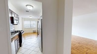 Located at 2175 Hudson Terrace in Fort Lee, NJ, this well-appointed two-bedroom, two-bathroom residence offers a thoughtfully designed single-floor layout. The spacious living room is a standout feature, showcasing classic parquet hardwood flooring that extends throughout the main living areas, complemented by bright white walls and large windows that invite abundant natural light. Sliding doors lead directly to a private patio, seamlessly connecting indoor and outdoor living. The galley-style kitchen is efficiently designed with rich dark wood cabinetry, granite-style countertops, a tile backsplash, and a full suite of stainless steel appliances, including a gas range, microwave, and refrigerator. Large-format tile flooring grounds the kitchen space. A dedicated dining area sits adjacent, providing a natural flow for everyday living and entertaining. The generously sized primary bedroom features the same warm parquet flooring, a walk-in closet, and direct access to an en-suite bathroom equipped with a vanity, mirror cabinet, and glass-door shower. The second bathroom offers a full tub-shower combination with tile surround. Three closets throughout the unit provide ample storage. The entrance hallway connects all spaces with ease, completing this functional and comfortable home.