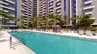 Located at 201 Clearwater Dr in West Palm Beach, Florida, this outdoor amenity level offers a resort-style pool deck designed for relaxation and leisure in a lush tropical setting. The centerpiece is a generously sized swimming pool with crystal-clear turquoise water, accessible via built-in entry steps and handrails, and framed by a broad, light-toned tile surround. Rows of cushioned lounge chairs and striped chaise lounges line the pool deck, providing ample space for sunbathing, while private shaded cabanas offer a more secluded retreat. Surrounding the pool, tall swaying palm trees and carefully curated tropical plantings create a verdant, resort-like atmosphere that evokes the feel of a South Florida oasis. A dedicated outdoor lounge area features modern, neutral-toned sectional sofas and accent tables arranged on large-format porcelain tile, ideal for socializing or unwinding beneath the open sky. The space is framed by the soaring façade of a contemporary high-rise tower, whose balconies and floor-to-ceiling glass windows overlook the pool below. The overall design seamlessly blends modern architectural elements with lush, tropical greenery, creating an inviting and sophisticated outdoor environment well-suited to the South Florida lifestyle.