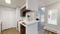 Located in the Woodland Hills neighborhood of Colorado Springs, this two-story home offers a thoughtfully designed layout spread across two levels. The main level features wood-look plank flooring throughout, creating a cohesive and clean aesthetic. The kitchen is equipped with dark espresso cabinetry, light stone-look countertops, white appliances including a refrigerator and dishwasher, and a peninsula with a double sink that opens directly to the living area. A skylight above the kitchen fills the space with natural light, enhancing the bright, airy atmosphere. The living room impresses with soaring vaulted ceilings and a sliding glass door that leads to an outdoor balcony, bringing in abundant natural light and views of surrounding greenery. A half bathroom on the main level features the same dark cabinetry, a framed mirror, and wood-look flooring. A carpeted staircase leads to the upper level, where the bedrooms are finished with plush carpet and ceiling light fixtures. One bedroom features a uniquely angled skylight window, adding architectural character. The upper-level full bathroom mirrors the main-floor finishes with dark cabinetry and light countertops.