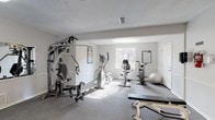 Located at 1601 Hillcrest Road in Mobile, Alabama, this fitness center offers a dedicated, single-floor space designed to support a well-rounded exercise routine. The facility is laid out across multiple connected areas, each serving a distinct workout purpose.

The main exercise room features neutral grey walls, durable carpet flooring, and a textured ceiling with overhead and natural lighting supplied by several windows. Strength training is supported by a multi-station cable machine, a Cybex adjustable bench, and a stability ball, while a reference chart on the wall aids in proper exercise form. Cardio equipment includes an elliptical trainer, a recumbent stationary bike, and a Star Trac treadmill, all positioned to take advantage of available natural light from exterior-facing windows.

The entry and transition area includes safety signage, a fire extinguisher, and clearly posted fitness center rules and guidelines. A hallway leads to additional utility spaces, including what appears to be a restroom or changing area with tile flooring.

The overall ambiance is clean, functional, and well-organized, with a straightforward layout that maximizes usable floor space. The facility is open 24 hours and requires an amenity key for access, making it a convenient option for residents seeking a reliable on-site workout space.