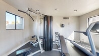 Located at 2020 E Broadway Rd in Tempe, Arizona, this fitness center is a well-equipped, single-room exercise facility designed to support a comprehensive workout routine. The space features durable dark rubber flooring throughout, providing a safe and practical surface suited for a variety of exercises. Natural light filters in through multiple windows along one wall, offering views of the surrounding Tempe landscape and creating a bright, energizing atmosphere.

The room is outfitted with a diverse selection of equipment to accommodate both cardio and strength training. Cardio options include Life Fitness elliptical trainers, a treadmill, and a stationary spin bike. For strength training, the facility features a multi-station cable machine, a functional trainer, a weight bench, and additional resistance equipment. A large wall-mounted mirror enhances the sense of space and allows users to monitor their form during workouts. A wall-mounted flat-screen television adds an entertainment option for those on cardio machines.

The room's neutral white walls, recessed lighting, and textured ceiling contribute to a clean, utilitarian aesthetic. Ventilation is provided via ceiling vents, and a smoke detector ensures safety compliance. The overall layout is efficient and thoughtfully arranged, maximizing the use of the available space while keeping pathways clear for comfortable movement between equipment.
