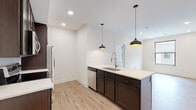 Located at 1050 N. 4th St in Columbus, Ohio's vibrant Short North neighborhood, this single-floor residence showcases a clean, contemporary design throughout. The kitchen is a standout feature, equipped with rich dark-espresso cabinetry, stainless steel appliances including a refrigerator, electric range, and built-in microwave, complemented by a white subway tile backsplash and light quartz countertops. A large central island with an integrated sink and stylish black pendant lighting above serves as both a functional workspace and a natural gathering point, flowing seamlessly into the open living area. Light-toned hardwood-style flooring runs throughout, enhancing the bright and airy atmosphere created by recessed lighting and natural light from black-framed windows. The bedrooms are well-proportioned, each featuring large windows with views of the surrounding neighborhood and clean neutral walls. The bathroom is finished to a high standard, with large-format white tile flooring, dark vanity cabinetry with a white countertop, a wide mirror, and a glass-enclosed walk-in shower accented by slate gray subway tile. The overall design palette of white walls, dark wood tones, and light flooring creates a cohesive, modern aesthetic throughout the space.