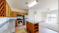 Located along US-34 in Greeley, Colorado, this single-story unit offers a functional and well-finished interior layout. The kitchen serves as a central highlight, featuring warm knotty alder cabinetry, granite countertops, a center island with additional storage and open shelving below, and a full suite of stainless steel appliances including a refrigerator, electric range, built-in microwave, and dishwasher. A decorative diamond-pattern wine rack is integrated into the upper cabinetry, adding a distinctive design detail. Light hardwood-style flooring runs throughout the kitchen and connects seamlessly to the adjacent living area.

The living space is carpeted and finished with neutral walls and a ceiling fan, creating a comfortable, open feel. A sliding glass door leads to an outdoor view of what appears to be a nearby body of water, providing a scenic natural backdrop. A secondary bedroom is also carpeted and receives natural light through a window with blinds.

The bathroom features a dual-sink vanity with granite countertops, warm wood cabinetry, and hardwood-style flooring. Additional storage is provided through a walk-in closet equipped with wire shelving, maximizing organizational capacity throughout the unit.