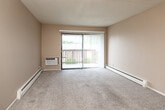 Located at 2800 Fleur Dr in Des Moines, Iowa, this two-bedroom, one-bathroom unit offers a practical and comfortable single-floor layout. The open living room is carpeted and features a sliding glass door with vertical blinds that opens to a private balcony, allowing natural light to fill the space. A ceiling fan and textured ceiling add functional character, while baseboard heating runs throughout the unit. The transition between the living area and entry is marked by warm hardwood-style flooring, which continues into the kitchen. The galley-style kitchen is well-appointed with honey oak cabinetry, marble-pattern countertops, a stainless steel sink, and black appliances including a gas range and refrigerator. Both bedrooms are carpeted and feature neutral walls, natural window light, and built-in closets with sliding panel doors offering organized storage. The second bedroom is served by its own baseboard heater and window with exterior views. The bathroom includes a full tub/shower combination, a white vanity with under-sink storage, a mirrored medicine cabinet with overhead lighting, and hardwood-style flooring. Overall, the unit presents a clean, functional layout well-suited for comfortable everyday living.