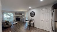 This single-floor residence offers a thoughtfully designed layout that balances comfort and functionality. The living room serves as the heart of the space, anchored by a striking stone fireplace with a raised hearth that adds rustic character to the room. Dark hardwood-style flooring runs throughout the main living areas, complementing the neutral gray walls and recessed lighting overhead. A sliding glass door floods the living room with natural light and provides direct outdoor access.

The kitchen is well-equipped for everyday cooking, featuring dark espresso cabinetry, stainless steel appliances including a refrigerator, range, microwave, and dishwasher, along with a white subway tile backsplash and light countertops. A compact high-top dining table with bar seating sits adjacent to the kitchen, making efficient use of the space.

The residence includes two bedrooms, both finished with plush carpeting and large windows fitted with blinds that allow for natural light while maintaining privacy. Each bedroom offers a calm, restful atmosphere with ample space for furnishings.

The bathroom features a full soaking tub with a shower combination, finished with neutral wall surrounds. Overall, the space presents a clean, modern aesthetic with warm accents throughout, creating an inviting and livable environment.