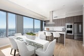 This elevated single-floor residence offers a seamless blend of contemporary design and urban luxury, defined by expansive floor-to-ceiling windows that frame breathtaking panoramic city and skyline views from nearly every room. Light hardwood flooring runs throughout, complementing the clean, neutral palette that gives the space a bright and airy character.

The gourmet kitchen is a standout feature, equipped with high-end stainless steel appliances including a large French door refrigerator, double wall ovens, and a gas cooktop set into a substantial center island with sleek stone countertops. Custom cabinetry in a rich wood-tone finish extends to the ceiling, providing generous storage, while a dramatic overhead range hood anchors the space. The kitchen opens toward dramatic city views, making it as functional as it is visually striking.

The living area is bathed in natural light, with corner window configurations offering expansive skyline vistas and a warm, inviting atmosphere. The bedrooms continue this elevated standard, each featuring large windows with far-reaching city views and hardwood floors. The bathrooms are finished with a modern sensibility, incorporating floating vanities, lit mirrors, stone tile flooring, and clean, minimalist fixtures. An entry area with a round mirror and natural wood console adds a refined transitional moment to the residence.