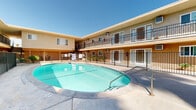 Located at 3636 Jackson St in Riverside, California, this multi-unit property presents a classic Southern California courtyard-style layout. The two-story stucco building is finished in warm earth tones, with each unit accessible via exterior walkways and iron-railed balconies that overlook the central courtyard below. Stairwells at each end of the building provide convenient access between levels, while individual unit entrances feature paneled doors with sidelight windows and wall-mounted HVAC units.

The centerpiece of the property is a generously sized oval swimming pool, positioned prominently within the enclosed courtyard and surrounded by a spacious concrete pool deck. The pool area is outfitted with patio furniture, including a shaded dining set beneath a large green umbrella, creating a comfortable outdoor gathering space. Iron fencing encloses the pool area for added safety and security.

Towering palm trees rise above the roofline, lending a distinctly Southern California ambiance to the outdoor space and providing a striking visual backdrop against the clear blue sky. Low-maintenance drought-tolerant landscaping, including agave and other native plantings, is thoughtfully integrated throughout the courtyard. The property's open-air design maximizes natural light and promotes a strong sense of community among residents.