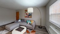 Located at 198 Crittenden Way in Rochester, NY, this single-floor unit offers a well-organized layout with a cohesive, contemporary design throughout. The kitchen is outfitted with white shaker-style cabinetry, light countertops, and a gray tile backsplash. Stainless steel appliances, including a range, over-the-range microwave, and dishwasher, provide a polished, functional workspace. Wood-look flooring runs through the main living areas, lending a clean and modern feel. The dining area benefits from a distinctive angled bay window that draws in natural light, complemented by a geometric gold pendant light that adds a stylish focal point. Adjacent to the dining space, the living room offers a comfortable, open setting with neutral walls and textured ceilings. The bedroom features wall-to-wall carpet, a window with outdoor views, and a baseboard heating unit. The bathroom is finished with a white vanity, a full tub-shower combination with built-in shelving, and light tile flooring. Overall, the unit presents a neutral, move-in-ready aesthetic with consistent finishes throughout.