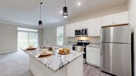 Located in Lewis Center, Ohio, this single-floor, 2-bedroom, 2-bathroom home offers a thoughtfully designed layout with a clean, contemporary aesthetic throughout. The entrance opens to a hallway with durable wood-look flooring that transitions into a bright, open-concept kitchen and living area. The kitchen is a standout feature, showcasing white shaker cabinetry, striking granite countertops, stainless steel appliances, a central island with a built-in sink, and stylish pendant lighting — all illuminated by abundant natural light from multiple windows. The living area extends seamlessly from the kitchen, offering a generous, carpet-floored space ideal for everyday living. Both bedrooms are carpeted and well-sized, with the spacious primary bedroom featuring a ceiling fan, access to a walk-in closet with wire shelving, and an en-suite bathroom. Both bathrooms are finished with white vanity cabinetry, granite countertops, wood-look vinyl flooring, and large mirrors. One bathroom includes a shower/tub combo, while the other features a glass-enclosed walk-in shower. Additional highlights include six closets for ample storage, a dedicated laundry area, a utility room, and a private patio for outdoor enjoyment.