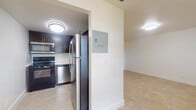 Located at 1210 NW 13th St in Boca Raton, Florida, this single-story unit presents a clean, functional layout with a neutral color palette and consistent light-toned tile flooring throughout. The space is thoughtfully organized across several rooms connected by a central corridor, as seen in the 3D floor plan overview.

The kitchen is a standout feature, equipped with dark espresso cabinetry, stainless steel appliances including a refrigerator, range, built-in microwave, and dishwasher, complemented by light quartz countertops and a sleek glass tile backsplash. The layout is efficient and well-appointed for everyday use.

The living and bedroom areas are generously proportioned, featuring bright white walls, ample ceiling lighting, and neutral tile flooring that adds a sense of continuity throughout. The entry area includes windows with blinds, allowing natural light to filter in while maintaining privacy.

The bathroom is finished with warm beige tile surrounding a full tub-shower combination, a dark wood vanity with quartz countertop, and a large mirror, creating a polished and cohesive aesthetic. Overall, the space offers a clean, move-in-ready environment with modern finishes throughout.