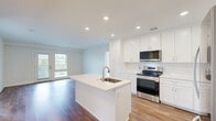 Located at 138 Mt Auburn Ave in Auburn, Maine, this single-floor, three-bedroom, two-bathroom residence offers a well-planned layout with a clean, modern aesthetic throughout. The open-concept kitchen and living area serves as the heart of the home, featuring rich hardwood-style flooring, recessed lighting, and abundant natural light from a door and adjacent window that open to an outdoor view. The kitchen is outfitted with crisp white shaker cabinetry, white quartz countertops, a subway tile backsplash, stainless steel appliances including an electric range and over-the-range microwave, and a central island with an undermount sink — ideal for both cooking and casual dining. The spacious primary bedroom includes hardwood-style flooring and direct access to a walk-in closet with wire shelving. Additional bedrooms feature plush carpet and bright windows. The two bathrooms are finished with classic black-and-white mosaic tile floors and gold-toned fixtures; one includes a soaking tub with tiled surround, while the other features a walk-in shower. Neutral walls and consistent finishes throughout lend the home a cohesive, move-in-ready feel.