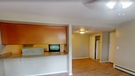 Located at 969 W Main Rd in Middletown, Rhode Island, this 690-square-foot, one-bedroom, one-bathroom apartment offers a practical and well-organized single-floor layout. The open-concept living room and kitchen area serves as the heart of the unit, featuring light hardwood-style flooring, a ceiling fan with integrated lighting, and baseboard heating. A wall-mounted AC unit provides additional climate control. The kitchen is equipped with warm wood cabinetry, granite-style countertops with a breakfast bar overhang, black appliances including a refrigerator and dishwasher, and durable hardwood-style flooring. The 200-square-foot primary bedroom includes a ceiling fan, hardwood-style flooring, and a window with outdoor views of greenery, filling the room with natural light. A dedicated closet provides convenient storage. The bathroom features a full tub and shower combination, a white vanity with a stone-style countertop, wood-look tile flooring, and a tile ceiling. Neutral beige tones are carried throughout the unit, creating a cohesive and calm ambiance. The floor plan also reveals a well-utilized layout that maximizes the available square footage, making this apartment an efficient and comfortable living space.