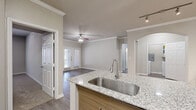 This single-story, 3-bedroom, 2-bathroom home offers a thoughtfully designed layout with modern finishes throughout. The open-concept living room is anchored by hardwood-style flooring, crown molding, a ceiling fan, and a set of French doors that invite natural light and provide outdoor access. The kitchen flows seamlessly into the living area and features a peninsula island with granite countertops and an undermount stainless steel sink, warm wood cabinetry, and a full suite of stainless steel appliances including a range, microwave, and refrigerator. Track lighting and a mirrored accent wall add a contemporary touch. The primary bedroom is generously sized with direct access to an en-suite bathroom, which includes a granite-topped vanity with wood cabinetry, wood-look tile flooring, and a glass-enclosed shower. The two additional bedrooms feature plush carpet, large windows with natural light, and ceiling fans. A dedicated laundry room, multiple closets, and two hallways enhance daily functionality. Neutral tones, crown molding, and consistent finishes create a cohesive, comfortable ambiance throughout the home.