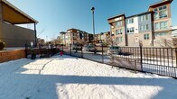 Located at 7338 S Havana St, this outdoor dog park is a dedicated amenity serving the surrounding residential community. The park is fully enclosed by sturdy black metal fencing, providing a secure environment for pets to roam freely. The open grounds offer ample space for dogs to run and play, with the area defined by low retaining walls and landscaped borders featuring ornamental shrubs and young trees.

A standout feature of the park is the covered pergola structure positioned at one end, providing shade and shelter for pet owners during all seasons. Flanking the pergola are benches, offering comfortable seating for visitors. An additional seating table is also present within the park area.

The park benefits from excellent natural light and open sky views, with the surrounding modern multi-story residential buildings serving as a backdrop. The community's contemporary architectural design — characterized by stone cladding, large windows, and warm wood-toned accents — frames the park on multiple sides. Street lighting poles are present within and adjacent to the park, ensuring visibility during evening hours.

The surrounding streetscape and parking areas are easily accessible, making this a conveniently located amenity for residents of the community.
