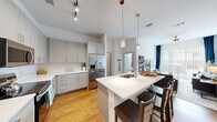 Located at 801 Wellborn Rd in College Station, TX, this well-appointed unit offers four bedrooms, four full bathrooms, and a thoughtfully designed single-floor layout. The open-concept kitchen is a standout feature, showcasing gray shaker-style cabinetry, white quartz countertops, a stainless steel appliance suite including a French door refrigerator and range, and a central island with a built-in sink and bar seating — illuminated by stylish pendant lighting and track fixtures above. Warm hardwood-style flooring flows throughout the main living areas, complementing the bright, clean aesthetic. The living room is generously sized, featuring a ceiling fan, sliding glass doors that invite natural light, and ample space for comfortable furnishings. Each bedroom offers plush carpeting, dedicated closet space, and high ceilings that enhance the sense of openness, with the primary bedroom providing notable square footage. The four bathrooms are uniformly finished with white subway tile, light cabinetry, quartz vanities, and hardwood-style flooring. An in-unit stacked washer and dryer adds everyday convenience. The overall design is modern and cohesive, with a neutral palette throughout.
