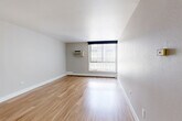 Located in Denver's desirable Congress Park neighborhood, this one-bedroom, one-bathroom residence offers a practical and well-appointed single-floor layout. Light-toned hardwood-style flooring runs consistently throughout, lending warmth and visual continuity to the space.

The combined kitchen and living area forms the heart of the home. The kitchen is outfitted with stainless steel appliances — including a refrigerator, dishwasher, microwave, and electric range — complemented by white cabinetry that extends to the ceiling for ample storage, and light countertops that keep the space feeling clean and bright. The adjacent living room is generously proportioned, featuring large windows fitted with vertical blinds that invite natural light, along with a wall-mounted air conditioning unit and baseboard heating for year-round comfort.

The bedroom is a comfortable, private retreat featuring a ceiling fan, two closets, and hardwood-style flooring that matches the rest of the unit. The bathroom includes a tiled shower-tub combination, a dark-accented countertop, and consistent flooring throughout.

Clean, neutral gray walls throughout the residence provide a versatile backdrop, while the open corridor connecting the rooms enhances the sense of flow and space within this efficiently designed home.