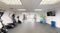 Located at 4314 Ginger Cove Dr in Tampa, FL, this fitness center offers a well-organized, single-floor layout designed to accommodate a full range of workout needs. The space is divided into distinct functional zones, creating a structured yet open environment for exercise.

The cardio area features multiple treadmills and elliptical machines positioned along large windows that invite abundant natural light and provide pleasant outdoor views of the surrounding greenery. Full-length mirrors along the walls enhance the sense of openness throughout this section.

The strength training zone houses a multi-station cable machine and a variety of weight training equipment, including an adjustable bench, providing ample options for resistance-based workouts. A dedicated wall-mounted storage rack holds stability balls and weighted medicine balls, supporting functional fitness and flexibility training.

Durable rubber flooring covers the entire facility, providing safety and comfort underfoot. The drop ceiling with recessed panel lighting ensures consistent, bright illumination throughout all areas. Two storage closets offer convenient space for equipment and supplies, while a dedicated entrance area facilitates smooth access to the facility.

The overall ambiance is clean, bright, and functional, with white walls and an uncluttered layout that promotes an efficient and motivating workout environment.