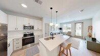 Located at 104 W Main St in Edmond, Oklahoma, this well-appointed 2-bedroom, 1-bathroom residence offers a thoughtfully designed single-floor layout that maximizes every square foot. The open-concept kitchen and living area serves as the heart of the home, anchored by a sleek white quartz kitchen island with a matte black faucet and bar seating. The kitchen features crisp white shaker cabinetry with black hardware, stainless steel appliances including a refrigerator, range, and built-in microwave, and light hardwood-style flooring. Two globe pendant lights hang above the island, adding a modern, airy touch. The living room benefits from large windows that invite generous natural light and outdoor views, creating a warm and inviting atmosphere. The primary bedroom offers a carpeted floor, built-in closet with shelving, and direct access to the hallway. The bathroom is finished with a white quartz vanity, shaker-style cabinetry with black hardware, and a large frameless mirror, maintaining the clean, contemporary aesthetic found throughout the residence. The overall design is cohesive and modern, with a neutral palette of whites and soft grays that lends the space a bright, airy ambiance.
