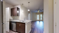 This well-appointed 1-bedroom, 1-bathroom unit in Austin, TX offers a thoughtfully designed single-level layout that maximizes functionality and comfort. The open-concept kitchen flows seamlessly into the living area, creating an inviting and connected space. The kitchen is equipped with stainless steel appliances — including a refrigerator, range, and microwave — rich dark espresso cabinetry, granite countertops, a double-basin sink, and elegant pendant lighting that adds a modern touch. Wood-style flooring runs throughout the main living areas, lending warmth and cohesion to the space.

The living area is bright and airy, benefiting from natural light through large windows and a glass-panel door that opens to the exterior, providing a private entryway. A ceiling fan enhances comfort in this central gathering space.

The bedroom features plush carpeting, a window with views of surrounding greenery, and ample wall space for flexible furnishing. The bathroom is finished with a dark-cabinet vanity, granite countertop, a large mirror with overhead lighting, and a walk-in shower. A dedicated in-unit laundry area with a washer and dryer adds everyday convenience. Neutral tones throughout create a clean, move-in-ready atmosphere.