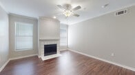 This single-floor residence offers a thoughtfully designed layout that balances comfort and functionality throughout. The living room serves as the focal point of the home, showcasing a classic white-tiled fireplace with a traditional mantel, rich hardwood-style flooring, crown molding, and a ceiling fan. Natural light filters in through multiple windows fitted with horizontal blinds, enhancing the room's bright and airy atmosphere. An entryway with recessed lighting and clean crown molding detail provides a welcoming introduction to the space. The open-concept dining and living area flows seamlessly toward the kitchen, which features a breakfast bar peninsula, light gray cabinetry extending to the ceiling, white countertops, and a full suite of white appliances including a refrigerator, electric range, built-in microwave, and dishwasher. Hardwood-style flooring continues throughout the common areas, while the bedrooms are finished with plush carpet and ceiling fans. The bedrooms offer generous proportions, with vertical blinds covering sliding door access and ample wall space. The bathroom is appointed with a soaking tub and shower combination featuring marble-look surround tiles and chrome fixtures. Track lighting accents and neutral gray-toned walls complete the cohesive, understated aesthetic throughout the home.