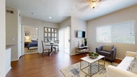 This single-story residence offers a thoughtfully designed layout that balances comfort and functionality. The living room serves as the heart of the home, featuring warm hardwood-style flooring, a ceiling fan, and a large window that fills the space with natural light. A wall-mounted TV, a cozy sofa, accent chair, and a gold-framed coffee table complete the inviting atmosphere. A sliding glass door provides access to an outdoor area, enhancing the sense of openness.

The kitchen is efficiently designed with an open peninsula layout, white cabinetry, stainless steel appliances including a range, microwave, and refrigerator, and a dual-basin sink — all finished with neutral countertops that complement the overall color palette.

Adjacent to the living area, a dedicated dining nook offers space for a small table and chairs beneath a decorative mirror. The bedroom is a serene retreat, carpeted for comfort and fitted with a ceiling fan, a generous window, and access to a spacious walk-in closet with built-in shelving and hanging rods on multiple walls.

The bathroom features a combination tub and shower with clean white tile surround, hardwood-style flooring, and ample towel storage. A dedicated in-unit laundry room with side-by-side washer and dryer and overhead shelving adds exceptional everyday convenience.