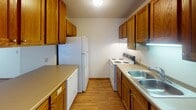 Located at 1401 Namekagon St in Hudson, Wisconsin, this single-floor unit offers a functional and comfortable layout across several well-defined living spaces. The open living area is a highlight, combining durable hardwood-style flooring with plush carpeting, a large window dressed with vertical blinds that invites abundant natural light, and a wall-mounted air conditioning unit alongside baseboard heating for year-round climate control. A textured ceiling adds character to the bright, neutral-toned walls throughout.

The kitchen is efficiently designed with warm oak cabinetry lining both sides, providing ample storage. White appliances — including a refrigerator, electric range, and dishwasher — are complemented by a double-basin sink and a built-in breakfast bar or pass-through counter, connecting the kitchen to the main living and dining area.

The bedrooms are carpeted for comfort, each featuring windows with horizontal blinds, baseboard heating, and overhead lighting. The rooms are well-proportioned with clean, neutral walls ready for personalization.

The full bathroom is neatly appointed with a wide vanity topped by a bright five-bulb light bar, a large mirror, wood-toned cabinetry beneath the sink, and a shower-tub combination. The overall design throughout the unit is practical and move-in ready, offering a clean, well-maintained living environment.