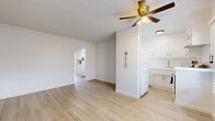 Located on Zelzah Avenue in the Porter Ranch neighborhood of Los Angeles, this single-story 2-bedroom, 1-bathroom home offers a thoughtfully organized layout with a bright, clean aesthetic throughout. Light-toned wood laminate flooring runs continuously across the living spaces, creating a cohesive and airy feel. The living room is a generous open space featuring crown molding, a ceiling fan with integrated lighting, and a textured ceiling, providing a comfortable area for daily living. It flows naturally toward the kitchen, which is neatly appointed with white cabinetry, a countertop sink, and a full-size refrigerator — all contributing to an efficient and functional cooking space. Two hallways connect the main living area to the private sleeping quarters. The primary bedroom is a well-sized room featuring mirrored sliding closet doors that add a sense of depth, while the second bedroom includes a dedicated walk-in closet and a window with horizontal blinds that frame views of surrounding greenery. The full bathroom is finished with light tile flooring, a white vanity with cabinet storage, and a shower-tub combination, maintaining the home's clean, white palette. Overall, the space presents a simple, functional, and well-maintained interior suited for comfortable everyday living.