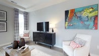 This single-floor residence is thoughtfully designed with a contemporary aesthetic, featuring light hardwood-style flooring and a neutral grey-and-taupe color palette that flows consistently throughout. The living room offers a bright, open feel with tray ceiling detailing, natural light from draped windows, and ample space for comfortable seating arrangements. A secondary sitting room provides an intimate retreat, bathed in natural light from dual windows framed by patterned drapes.

The kitchen is outfitted with dark espresso cabinetry, light stone countertops, stainless steel appliances, and a central island. A sliding glass door opens directly onto a private balcony overlooking a wooded outdoor view, blending indoor and outdoor living seamlessly.

The primary bedroom features a tray ceiling with a ceiling fan, large windows, and direct access to an en-suite bathroom equipped with a dual-sink vanity, dark cabinetry, stone countertops, and a glass-enclosed shower. A second bedroom includes a walk-in closet with built-in organization. A secondary full bathroom offers a white vanity with stone countertops and clean tile flooring, providing practical functionality throughout the residence.