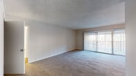 Located at 6615 The Lakes Dr in Raleigh, NC, this single-floor residence offers a well-organized layout designed for comfortable everyday living. The spacious living area is finished with plush wall-to-wall carpeting and a textured ceiling, creating a warm and inviting atmosphere. A large sliding glass door fitted with vertical blinds opens to a private balcony, allowing natural light to fill the room and providing an easy connection to the outdoors. A ceiling fan in the adjoining area adds to the comfort of the space. The layout flows naturally from the living area toward the kitchen and entryway, which are visible through a central dividing wall. The kitchen is equipped with black appliances, including an electric range with overhead ventilation, a dishwasher, and a stainless steel sink, all complemented by crisp white cabinetry and speckled quartz-style countertops. The bedroom features soft carpeting, a window with blinds that brings in natural light, and a textured ceiling consistent with the rest of the unit. The bathroom includes a white vanity with quartz-style countertops, a mirrored medicine cabinet with lighted fixture, and a separate tub/shower combination with built-in shelving, all set on wood-look flooring. The unit presents a clean, functional, and well-maintained living environment throughout.