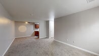 Located at 5179 Dempster Dr in Columbus, Ohio, this single-floor home offers four bedrooms, two bathrooms, a living room, and a kitchen connected by a central hallway. The open living area features neutral gray walls and wall-to-wall carpet, creating a clean and functional space. Natural light enters through windows with blinds, and a front entry door provides direct access to the living room. The galley-style kitchen is well-appointed with rich, warm-toned wood cabinetry, white countertops, a single-basin sink, and black appliances including a range and refrigerator, all set on wood-look vinyl flooring. The four bedrooms are carpeted and finished with the same neutral gray palette, offering a calm and consistent aesthetic. Several bedrooms include built-in closets with shelving, providing practical storage. The primary bedroom offers a comfortable footprint with its own closet space. Both bathrooms feature wood-look vinyl flooring, warm wood vanities with white countertops, and full tub-shower combinations with clean white surrounds. The hallway connects all rooms efficiently, making the layout easy to navigate throughout the home.