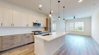 Located in Austin, TX, this well-designed 2-bedroom, 2-bathroom residence offers a modern aesthetic with thoughtful finishes throughout. The open-concept kitchen and living area serves as the heart of the home, featuring a large center island with a striking quartz countertop, an undermount sink, and elegant globe pendant lighting. The kitchen is outfitted with two-tone cabinetry — light upper cabinets paired with warm wood-toned lower cabinets — complemented by a white subway tile backsplash and a full suite of stainless steel appliances, including a gas range, microwave, and French door refrigerator. Light wood-style flooring runs throughout the entire space, lending warmth and continuity. The living area is bright and airy, with large windows and a ceiling fan that invite natural light and outdoor views. The spacious primary bedroom includes its own en-suite bathroom, which features a quartz-topped vanity with wood-grain cabinetry, a glass-enclosed shower, and a walk-in closet with built-in shelving. The second bedroom also offers closet storage with double-door access and matching flooring. The second bathroom mirrors the refined design of the primary bath, complete with a marble-veined quartz vanity and generous cabinetry. Clean lines and neutral tones create a cohesive, contemporary ambiance throughout.