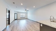 Located at 115 SW Eagles Pkwy in Grain Valley, Missouri, this single-floor unit presents a clean, contemporary design with thoughtfully selected finishes. The open-concept living and kitchen area serves as the heart of the space, anchored by light-toned hardwood-style flooring that runs throughout the main living areas. Recessed lighting and a ceiling fan overhead enhance both the brightness and comfort of the room, while windows and a glass-panel door allow natural light to fill the space.

The kitchen is well-appointed with gray shaker-style cabinetry, a white subway tile backsplash, and a full suite of stainless steel appliances, including a refrigerator, electric range, and built-in microwave. A peninsula with a bold navy blue base and granite countertop provides additional prep space and connects seamlessly to the living area.

The bedroom features plush carpet flooring, a ceiling fan, and a window dressed with blinds. It connects directly to a full bathroom finished with granite countertops, a wide vanity mirror, and wood-look flooring. A closet offers convenient additional storage. The neutral color palette and dark door trim throughout lend the space a modern, cohesive aesthetic.