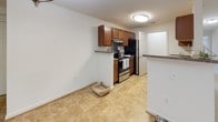 This single-floor residence offers a thoughtfully designed layout with a comfortable mix of living, sleeping, and utility spaces. The generously sized living room features plush carpeting, a tray ceiling with a ceiling fan, and multiple windows that invite abundant natural light and views of surrounding greenery, creating a bright and airy atmosphere. The kitchen is equipped with rich, warm-toned cabinetry, granite-style countertops, stainless steel appliances including a range and refrigerator, and tile flooring that extends throughout the space. A breakfast bar adds both functionality and an informal dining option. The bedrooms are finished with soft wall-to-wall carpeting and windows fitted with blinds for privacy and light control, offering versatile and comfortable spaces. The bathroom is well-appointed with a vanity featuring warm wood cabinetry and a stone-finish countertop, a full tub and shower combination with crisp white surrounds, hardwood-style flooring, and a multi-bulb light fixture above a large mirror. A dedicated laundry area accommodates a full-size washer and includes overhead shelving for additional storage. Throughout, the space maintains a clean, neutral palette with white walls and consistent finishes, providing a cohesive and welcoming environment.