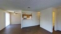 This two-floor residence offers a straightforward and functional layout designed for comfortable everyday living. The main living area is grounded by rich, dark hardwood flooring that extends throughout, creating a warm and cohesive feel. A ceiling fan overhead provides both light and airflow, contributing to the room's practical comfort.

A defining architectural feature of the main level is the pass-through kitchen, which opens from the living space via a half-wall counter. The kitchen is equipped with warm wood cabinetry, a white refrigerator, a range with an overhead ventilation hood, and a built-in fluorescent light fixture that brightens the workspace. The counter pass-through adds a sense of connectivity between the kitchen and living areas without fully opening the two spaces.

The ceilings throughout feature a textured finish, and HVAC vents are integrated into the ceiling for efficient climate control. A door positioned near the kitchen provides access to additional areas of the home. The overall aesthetic is clean and neutral, with white walls that allow for easy personalization. Spanning two floors, the home offers separation between living and private spaces, making it a well-organized and livable environment.