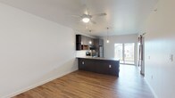 Located at 1500 NW A St in Bentonville, Arkansas, this modern single-floor unit offers a thoughtfully designed open-concept layout with contemporary finishes throughout. Warm hardwood-style flooring flows seamlessly across every room, creating a cohesive and inviting atmosphere.

The kitchen serves as a central focal point, showcasing dark matte cabinetry with wood accent panels, a white subway tile backsplash, and a suite of stainless steel appliances including an electric range and refrigerator. A spacious island with a quartz-style countertop and double undermount sink doubles as a breakfast bar, while Edison-style pendant lights with distinctive red cords add an industrial-chic touch. The open-plan living area extends naturally from the kitchen, bathed in natural light from sliding glass doors that lead to a private balcony. A ceiling fan overhead provides comfort and airflow throughout.

The bedroom is a calm, well-proportioned retreat featuring a ceiling fan and a window with blinds that frame views of surrounding greenery. The entryway includes a built-in bench, adding a practical and welcoming touch upon arrival.

The bathroom is finished in a clean, modern aesthetic with a dual-sink vanity, quartz countertops, white cabinetry, and a fully tiled walk-in shower. Every detail reflects a commitment to contemporary style and functional living.