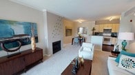 This thoughtfully designed single-floor residence offers a cohesive blend of comfort and modern style across its well-organized layout. The open-concept living and dining area serves as the heart of the home, anchored by a striking white-tiled fireplace with a sleek surround and accented by crown molding that frames the space with architectural detail. Plush carpeting and neutral tones create a warm, inviting atmosphere throughout.

The kitchen is both functional and visually appealing, featuring rich dark granite countertops, light maple cabinetry, a gas range, and a distinctive mosaic tile backsplash in cool blue and grey tones. A breakfast bar provides additional prep and seating space, while track lighting illuminates the room effectively.

Two generously sized bedrooms offer a peaceful retreat, each adorned with large windows that invite natural light and provide outdoor views. One bedroom features a spacious walk-in closet with built-in wire shelving, offering ample storage. A full bathroom with a soaking tub, bold green accent walls, and dark hardwood-style flooring completes the private quarters.

A separate living room area near the entryway opens to the outdoors via a sliding glass door, further enhancing the sense of light and connectivity to the exterior. The overall aesthetic is modern and cohesive, with a consistent use of teal, neutral, and warm tones throughout.
