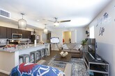 This single-floor unit offers a thoughtfully designed open-concept layout that seamlessly connects the kitchen, dining, and living areas. The kitchen is a standout feature, boasting granite countertops, dark espresso cabinetry, stainless steel appliances including a microwave and range, and a generously sized island with bar seating — ideal for casual dining or entertaining. Stylish pendant lighting illuminates the space, complementing the warm wood-look flooring that flows throughout the main living areas.

The living room is cozy and inviting, with a large flat-screen TV setup, natural light from a window with blinds, and thoughtful wall décor that adds personality to the space. A hallway connects the main living area to the private quarters of the unit.

Two well-proportioned bedrooms feature plush carpeting, ceiling fans, ample natural light from multiple windows, and space for both sleeping and study. Each bathroom is finished with tile flooring, dark vanity cabinetry, granite countertops, and a tub-shower combination. The unit also benefits from convenient in-unit storage and a clean, neutral color palette that creates a bright and welcoming atmosphere throughout.
