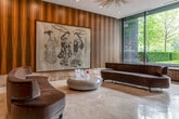 Located at 50 Hillsboro Ave in Toronto's prestigious Annex neighbourhood, this sophisticated lobby space offers a refined first impression with a seamlessly curated blend of luxury materials and contemporary design. The single-floor space is generously proportioned, providing an open, airy ambiance that immediately commands attention.

The interior is defined by striking bookmatched marble wall cladding in warm honey and gold tones, complemented by rich, vertically grained wood paneling that lends a sense of warmth and depth throughout. Polished large-format marble tile flooring reflects the recessed ceiling lighting, enhancing the sense of spaciousness and elegance.

A welcoming lounge area features sculptural, curved seating pieces in deep velvet and leather upholstery arranged around an organic stone coffee table, creating an inviting focal point. A large-scale framed artwork adds a cultural and artistic dimension to the space.

Floor-to-ceiling glass windows along one elevation flood the interior with natural light while offering serene views of the mature, tree-lined streetscape outside. A dedicated reception desk anchors one end of the lobby, while elevator bays clad in matching marble provide seamless connectivity. An eye-catching sputnik chandelier overhead adds a final touch of contemporary sophistication to this meticulously appointed space.
