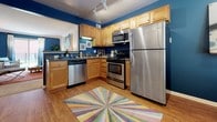 Located at 165 Kathann Dr in Hampton, Virginia, this single-floor residence offers a well-designed layout that balances comfort and style. The spacious living room serves as the heart of the home, featuring crown molding, a bold accent wall in deep navy blue, and a sliding glass door that opens to a private outdoor balcony, filling the space with natural light. The open sightline connects the living area to the kitchen, which is outfitted with light maple cabinetry, dark countertops, stainless steel appliances including a refrigerator, range, microwave, and dishwasher, and wood-look flooring under track lighting. The primary bedroom features a striking teal accent wall, plush carpeting, and windows that allow for ample natural light, creating a bold yet restful retreat. A second bedroom offers a quieter, neutral palette with soft carpeting and natural light from corner windows. The primary bathroom includes an extended vanity with warm wood cabinetry, a large mirror, and wood-look flooring, while the second full bathroom features a shower-tub combination, a single vanity, and matching wood-look flooring. The overall ambiance of the home is vibrant and well-appointed, with cohesive design choices that make each room feel intentional and inviting.
