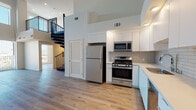 Located at 2783 Francis Ave in Los Angeles, CA 90005, this contemporary two-story residence showcases a thoughtfully designed open layout with modern finishes throughout. The main level features soaring double-height ceilings that create a striking sense of volume, anchored by a bold black spiral staircase that serves as a dramatic architectural focal point. Warm wood-look flooring extends seamlessly across both levels, contributing to a cohesive and inviting atmosphere. The kitchen is well-appointed with stainless steel appliances—including a gas range, microwave, and refrigerator—complemented by crisp white upper cabinetry, light blue-grey lower cabinets, a subway tile backsplash, and a dishwasher. Recessed lighting and large sliding glass doors allow natural light to fill the living area, which opens to views of the surrounding Los Angeles cityscape. The upper level offers open, versatile living space with recessed lighting and clean, neutral walls, ideal for a variety of uses. Two bathrooms provide modern functionality, each featuring floating white vanities, large mirrors, and wood-look tile flooring. One bathroom includes a full tub-shower combination with glass enclosure, while the other offers a half-bath configuration with a window for natural light. A bedroom on the upper level enjoys sweeping city and treetop views through a large window.