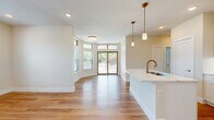 This thoughtfully designed 2-bedroom, 2-bathroom residence offers a comfortable and modern living experience on a single floor. The open-concept living and kitchen area forms the heart of the home, bathed in natural light through a wide bank of windows and glass doors that lead to an outdoor balcony with views of surrounding greenery. Warm hardwood flooring flows throughout the main living spaces, complementing the bright, neutral palette of the walls and trim.

The kitchen is well-equipped with white shaker cabinetry accented by gold hardware, a quartz waterfall island with an undermount sink, stainless steel appliances including a French door refrigerator, range, microwave, and dishwasher, and elegant gold pendant lighting overhead.

The primary bedroom is generously sized, featuring hardwood floors, recessed lighting, and a dedicated walk-in closet outfitted with built-in shelving and hanging rods for ample storage. The second bedroom offers plush carpeting, a ceiling fan, and a bright window. Both bathrooms are finished with clean tile work and brushed gold fixtures, with one featuring a full soaking tub and shower combination. The overall ambiance is clean, bright, and move-in ready.
