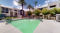 Located at 3411 16th Street in Phoenix, Arizona, this outdoor amenity space showcases a resort-style courtyard designed for relaxation and leisure under the Arizona sun. At the heart of the space is a generously sized swimming pool with a distinctive diamond-shaped design and clear, inviting water, surrounded by a wide concrete pool deck lined with lounge chairs for sunbathing.

Towering palm trees and mature shade trees frame the perimeter of the courtyard, providing natural beauty and a sense of privacy. A covered cabana anchors one side of the space, featuring a pitched wood-paneled ceiling, decorative striped curtains, and comfortable wicker lounge chairs with cushioned ottomans — ideal for shaded outdoor relaxation. The cabana area also includes bar-height seating, making it a versatile social gathering spot.

The surrounding landscape incorporates desert-friendly plantings, ornamental ironwork fencing, and well-maintained gravel beds, all consistent with the Southwest aesthetic. The multi-story buildings enclosing the courtyard feature a contemporary stucco exterior with bold architectural accents in navy and neutral tones. Ample natural light fills the space throughout the day, while the open-sky setting allows for sweeping views of the surrounding lush canopy and bright blue Arizona sky.