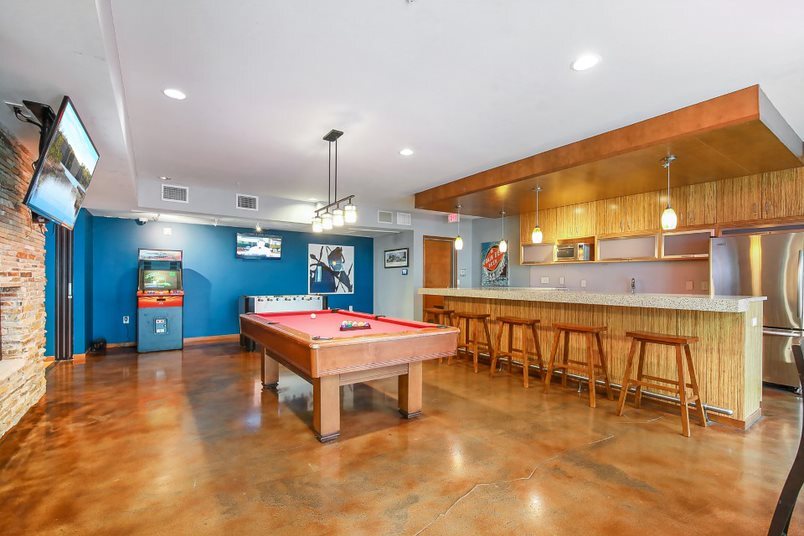 Community lounge with a pool table, foosball table, arcade game, and bar with stools.