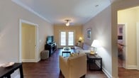 This single-floor residence offers a thoughtfully designed open-concept layout that seamlessly connects the living, dining, and kitchen areas. Rich hardwood-style flooring runs throughout the main living spaces, complemented by crown molding and warm neutral tones that create a cohesive and inviting ambiance.

The living room is a comfortable gathering space featuring a ceiling fan, recessed lighting, and French doors that invite natural light and provide outdoor access. The kitchen is fully equipped with stainless steel appliances — including a refrigerator, range, and microwave — set against granite countertops and warm wood cabinetry. A breakfast bar offers additional seating and connects the kitchen to the open living area. A dedicated dining space accommodates a full table and chairs.

The residence includes multiple bedrooms, each carpeted for comfort and outfitted with ceiling fans and natural light from windows with blinds. The bedrooms feature generous space for furnishings and offer a calm, restful atmosphere. Two bathrooms serve the residence; one features a double-sink vanity with granite countertops, while the second includes a shower-tub combination. Both bathrooms continue the hardwood-style flooring seen throughout the home, maintaining a consistent and polished aesthetic.