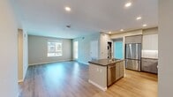 North Grove B2A is a well-appointed single-floor apartment in Riverside, California, offering 860 square feet of thoughtfully designed living space across three bedrooms and two bathrooms. The open-concept kitchen and living area serves as the heart of the unit, featuring light wood-style flooring, recessed lighting, and a sleek kitchen island with a stone countertop and undermount sink. The kitchen is outfitted with stainless steel appliances, a gas range, built-in microwave, and two-tone cabinetry with white upper cabinets and gray lowers, accented by a classic subway tile backsplash. The living area benefits from natural light through large windows and a glass door that opens to views of the surrounding community. The primary bedroom spans 140 square feet with plush carpeting, a dedicated closet, and direct access to a bathroom. Additional bedrooms are carpeted and feature windows with exterior views. Both bathrooms include tub/shower combos with tiled surrounds, vanities with dark countertops, and wood-style flooring. A hallway and closet provide additional storage. The exterior showcases a modern multi-story building with covered parking and landscaped grounds under sunny Southern California skies.
