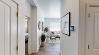 This single-story residence offers a thoughtfully designed layout that balances openness with defined living spaces. A welcoming hallway with wood-style flooring connects the main areas, with a bedroom visible off one side and the living room drawing the eye forward. The living room is generously proportioned, anchored by a large window with horizontal blinds that allows ample natural light to fill the space. Ceiling fans are present throughout, enhancing comfort and airflow. The kitchen features rich, dark wood cabinetry paired with light countertops and stainless steel appliances, including a range, microwave, and dishwasher. A dining area sits adjacent, providing a practical transition between cooking and gathering spaces. Both bedrooms are carpeted and well-sized, each accommodating full bedroom sets with ease. The primary bathroom includes a wide vanity with dark wood cabinetry, a large mirror, and elegant multi-bulb lighting. A second full bathroom features a tub-shower combination, single vanity with matching cabinetry, and a window for natural light. Throughout the residence, a consistent neutral color palette and clean finishes contribute to a cohesive, modern aesthetic.