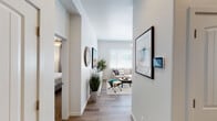 This single-story residence offers a thoughtfully designed layout that balances openness with defined living spaces. A welcoming hallway with wood-style flooring connects the main areas, with a bedroom visible off one side and the living room drawing the eye forward. The living room is generously proportioned, anchored by a large window with horizontal blinds that allows ample natural light to fill the space. Ceiling fans are present throughout, enhancing comfort and airflow. The kitchen features rich, dark wood cabinetry paired with light countertops and stainless steel appliances, including a range, microwave, and dishwasher. A dining area sits adjacent, providing a practical transition between cooking and gathering spaces. Both bedrooms are carpeted and well-sized, each accommodating full bedroom sets with ease. The primary bathroom includes a wide vanity with dark wood cabinetry, a large mirror, and elegant multi-bulb lighting. A second full bathroom features a tub-shower combination, single vanity with matching cabinetry, and a window for natural light. Throughout the residence, a consistent neutral color palette and clean finishes contribute to a cohesive, modern aesthetic.