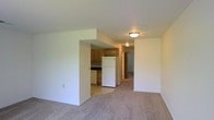 This two-floor residential space offers a straightforward and functional layout designed for comfortable everyday living. The main level features an open-concept design where the living area flows seamlessly into the kitchen, creating a cohesive and accessible floor plan. The living space is finished with neutral-toned carpeting that adds warmth underfoot, while clean white walls provide a bright and airy atmosphere throughout.

The kitchen is defined by warm wood-tone cabinetry that offers ample storage, paired with a dark countertop and essential appliances including a full-size white refrigerator and dishwasher. Flush-mount ceiling light fixtures provide consistent overhead lighting throughout the main level. A hallway visible from the main living area connects to additional rooms, suggesting a well-organized circulation path through the home.

The two-floor configuration provides a natural separation between living and private spaces, making the layout practical for a variety of occupants. The overall aesthetic is clean, simple, and move-in ready, with neutral finishes throughout that offer a versatile backdrop for personalization. The open sightlines between the living and kitchen areas enhance the sense of space and make the home feel welcoming and easy to navigate.