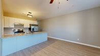 This single-story home is designed with a clean, modern aesthetic highlighted by light-toned luxury vinyl plank flooring that flows consistently throughout the entire space. The open-concept layout connects the kitchen and living area seamlessly, creating a spacious and functional common area. The kitchen is well-appointed with white shaker-style cabinetry, light granite countertops, stainless steel appliances including a French door refrigerator, electric range with overhead ventilation, and dishwasher. A peninsula with a built-in sink extends into the living area, offering casual seating and additional workspace. The living area features vaulted ceilings and a ceiling fan with a pendant light drop, adding an airy feel to the space. Bedrooms are generously sized, each equipped with ceiling fans and neutral gray walls that create a calm atmosphere. One bedroom benefits from dual windows that invite natural light. The bathroom includes a full tub-shower combo, white vanity with granite countertop, and coordinating flooring. A dedicated laundry room offers wire shelving, washer/dryer hookups, and ample utility space. Neutral warm-gray tones and white trim are consistent throughout, lending the home a cohesive, move-in-ready appeal.